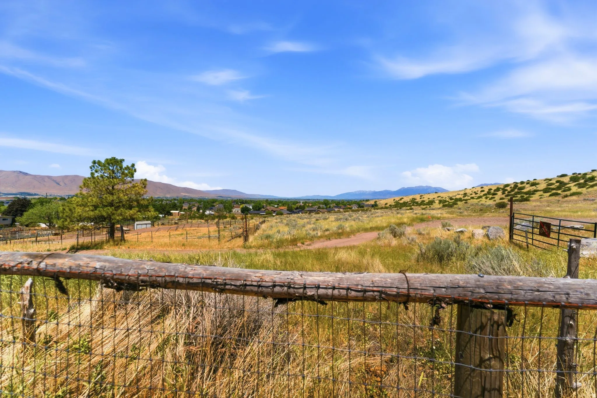 Expansive undeveloped land featuring a wire and wood-post fence, a metal gate, and distant mountain ranges
