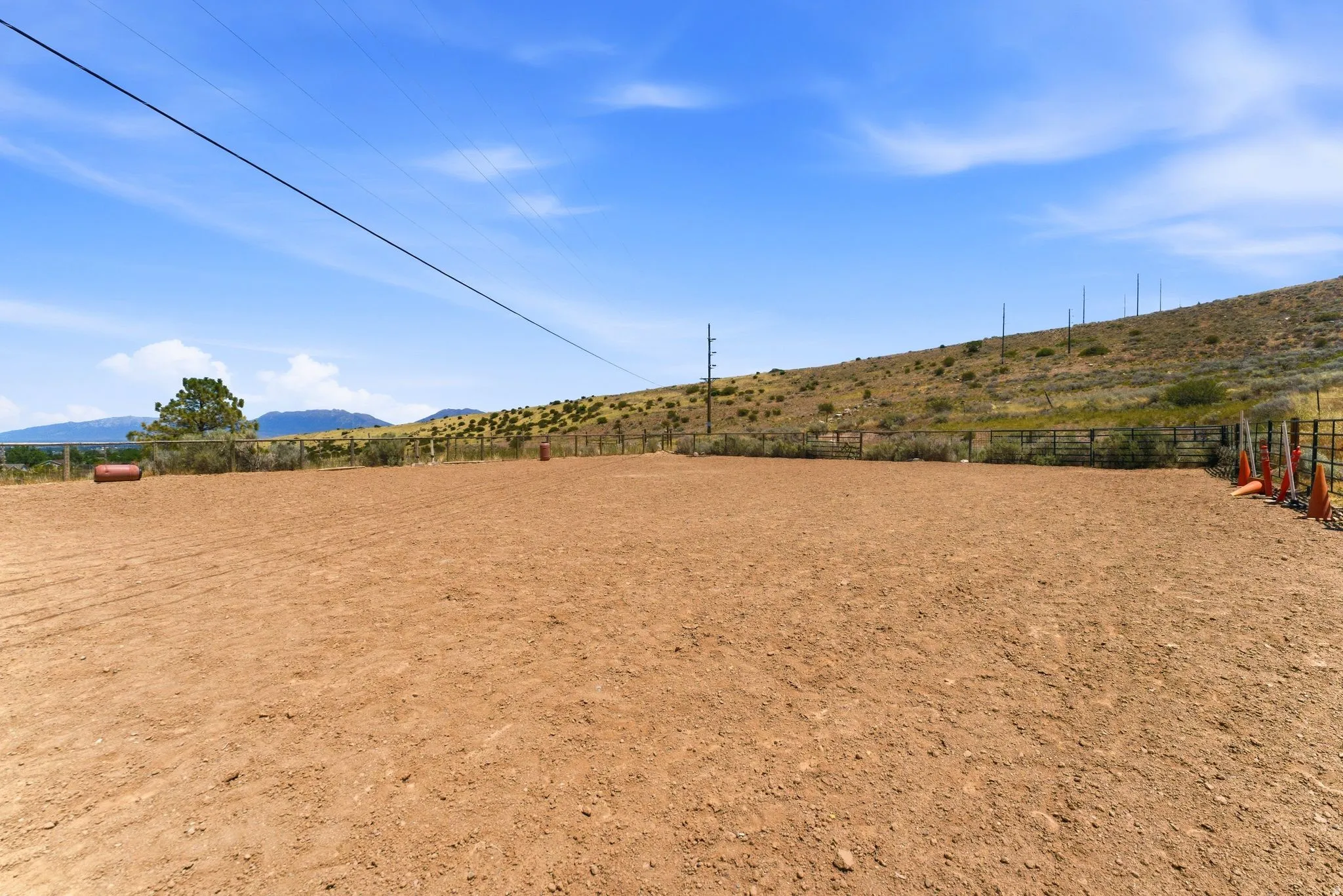 Expansive outdoor area featuring a graded dirt surface, perimeter fencing, and distant mountain scenery