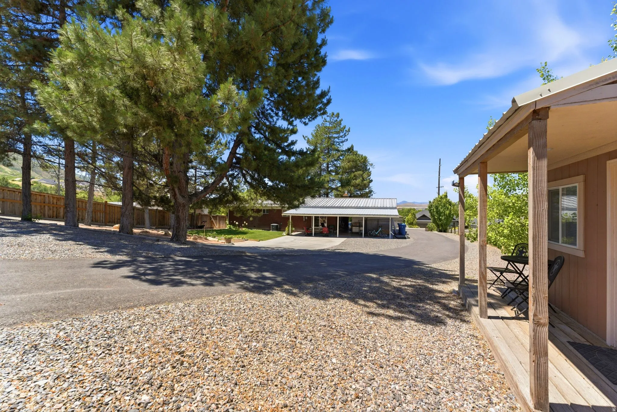 Property exterior featuring a covered porch with wooden posts, a gravel and asphalt driveway, and mature trees providing natural shade
