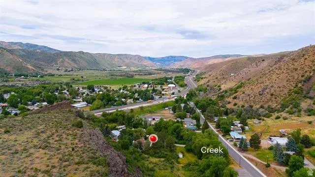 Expansive mountain valley landscape featuring a winding creek, mature trees, and a visible roadway