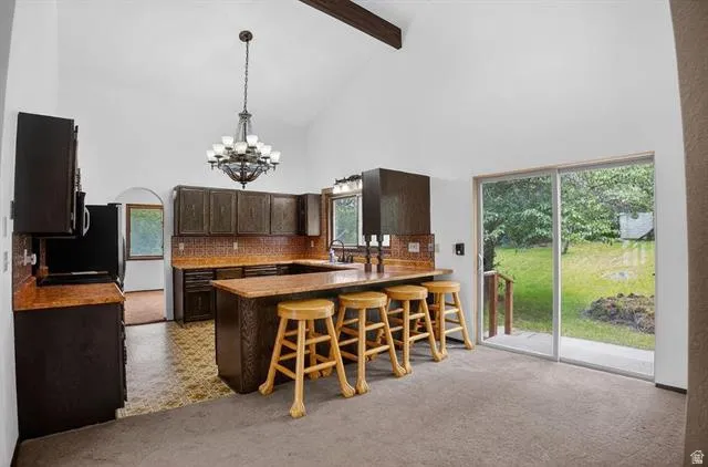 Vaulted ceiling kitchen featuring dark wood cabinetry, a breakfast bar, patterned tile backsplash, and an arched doorway