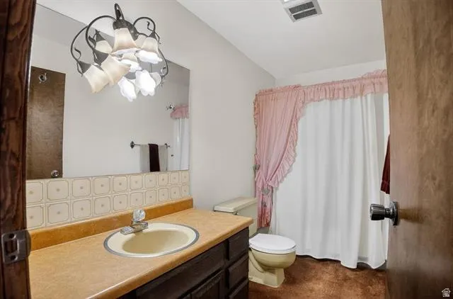 Bathroom featuring a single vanity with a laminate countertop and integrated sink, a large wall-mounted mirror, a patterned tile backsplash, and overhead lighting