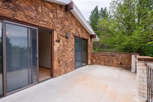 Expansive outdoor patio with concrete flooring, stone veneer exterior, a stone and brick half-wall, and dual sliding glass doors