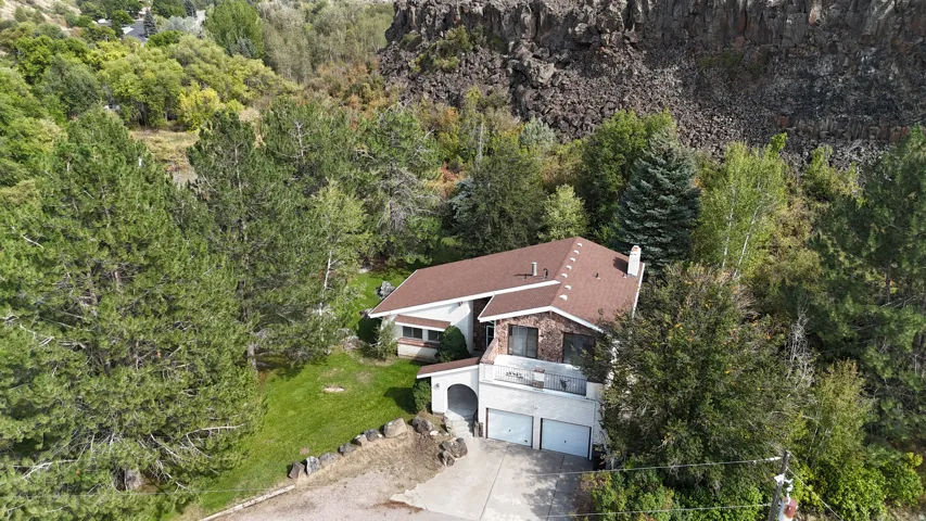 Multi-level exterior with a brown shingle roof, stone accents, two-car garage, and surrounding mature trees