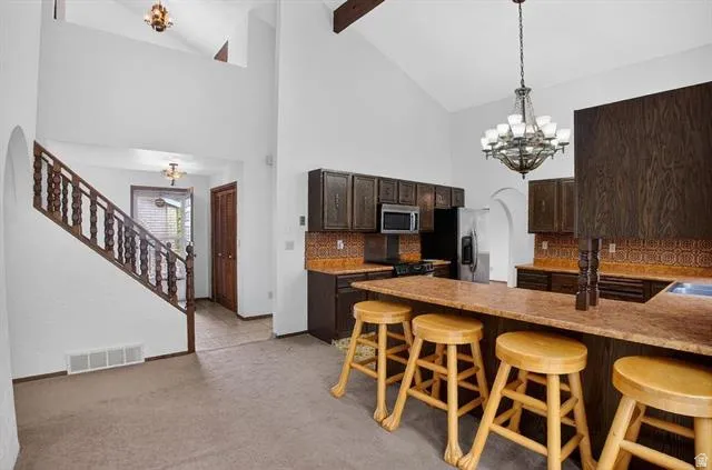Vaulted ceiling kitchen featuring dark wood cabinetry, an integrated breakfast bar, and a patterned tile backsplash