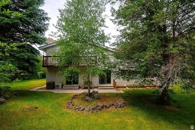 Expansive rear yard featuring mature trees, a manicured lawn, and a stone-edged planting area