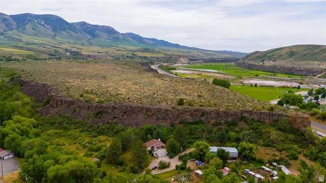 Expansive acreage featuring mountainous terrain, mature trees, a river, and a residential structure with an attached garage