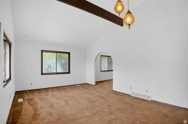 Spacious interior room with vaulted ceilings and exposed wood beam