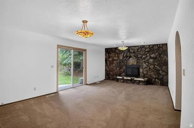 Spacious room featuring a prominent stone accent wall with a built-in fireplace, sliding glass doors providing access to the exterior, and two decorative ceiling light fixtures