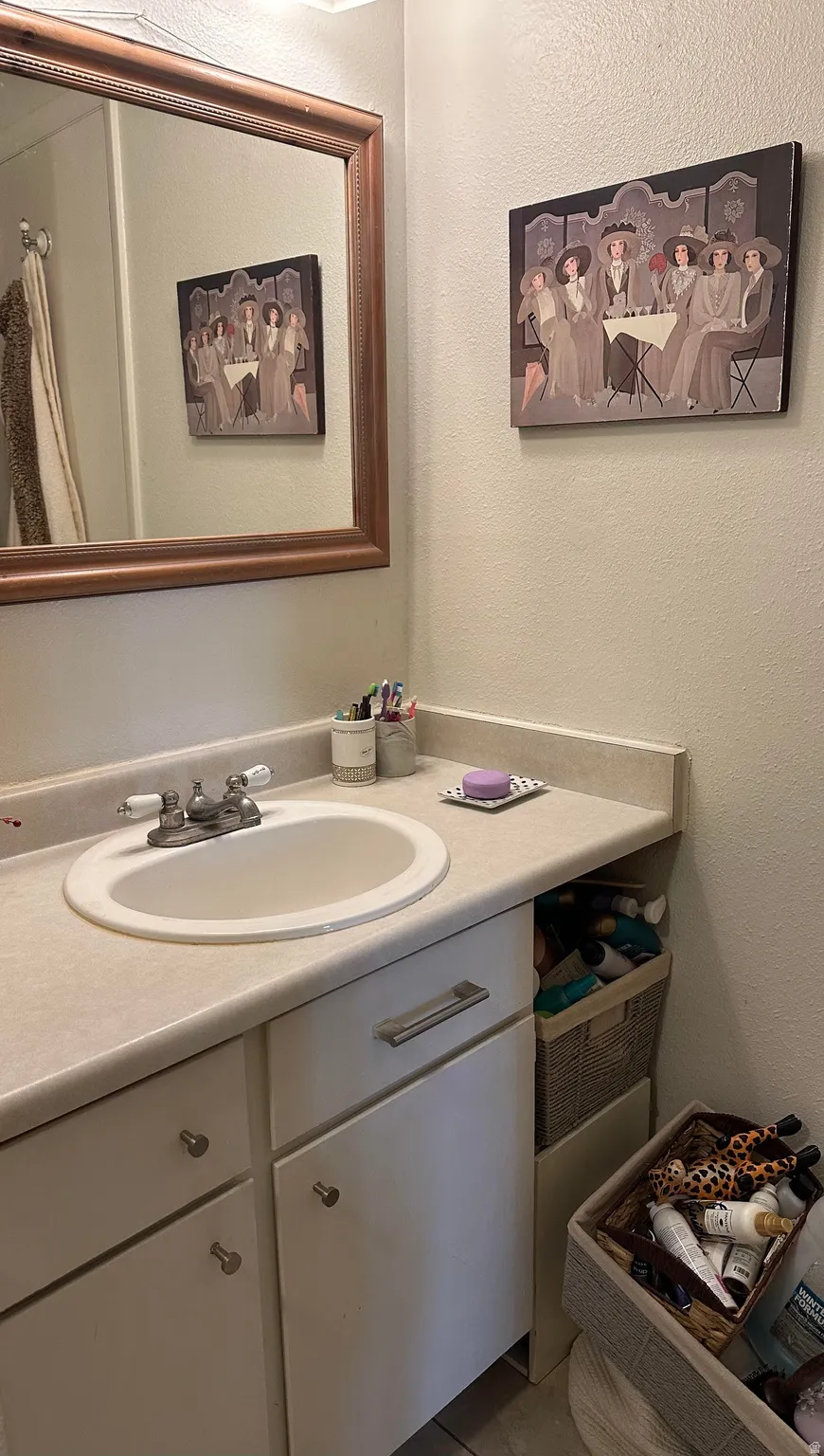 Bathroom vanity featuring a drop-in sink with a two-handle faucet, a light-toned countertop, and white cabinetry