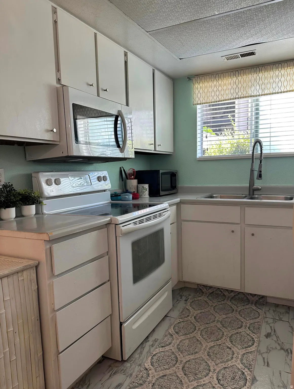 Kitchen featuring white cabinetry, light countertops, an electric range, an over-range microwave, and a double basin sink with a gooseneck faucet
