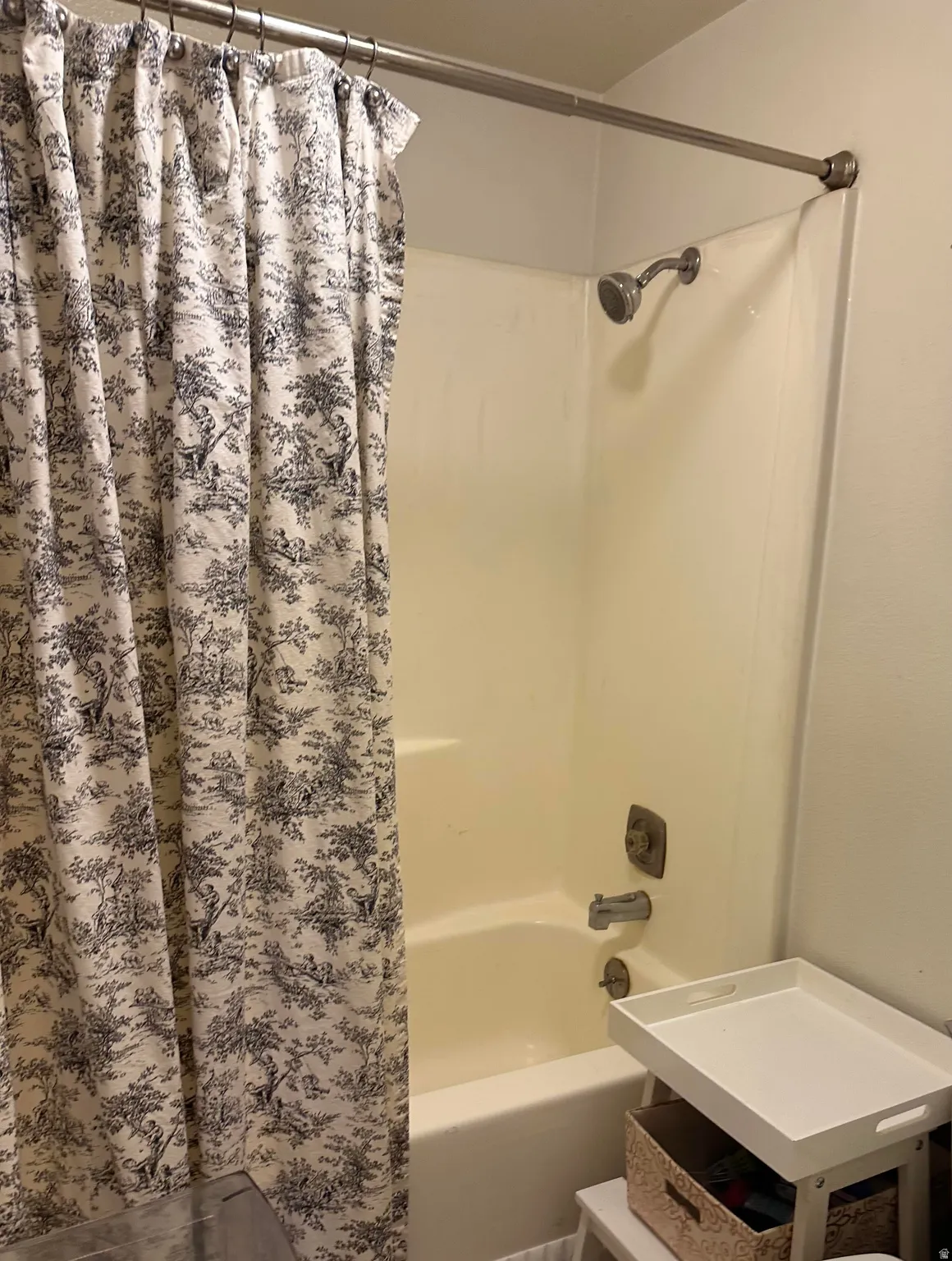 White bathtub and shower combination featuring a brushed nickel shower head and faucet