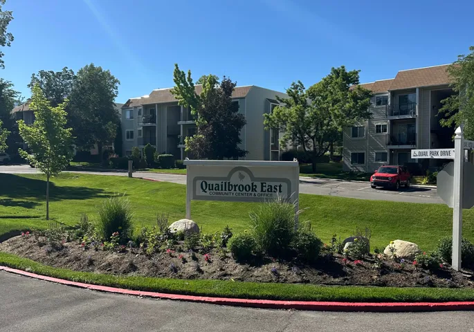 Landscaped entry featuring a community sign, mature trees, and manicured lawns