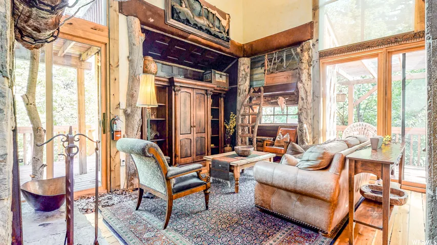 Vaulted living room featuring wood-finish flooring, exposed natural wood structural elements, custom built-in cabinetry, and expansive glass sliding doors opening to an outdoor deck