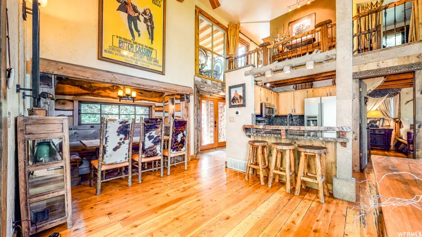 Open-concept living space with wood-finish flooring, a kitchen featuring a breakfast bar with stone accents, an adjacent dining area, and a lofted upper level with an iron railing