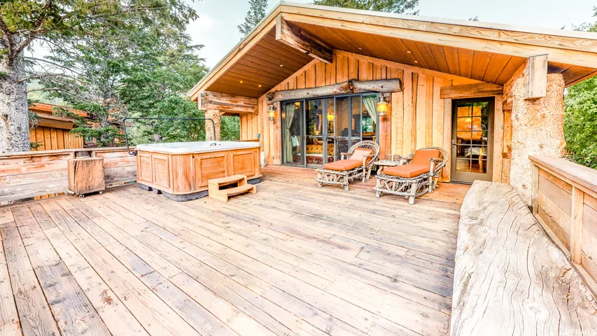 Expansive wood deck with a built-in hot tub, wooden railing, and direct access to the interior via a glass-paneled door and large sliding glass doors