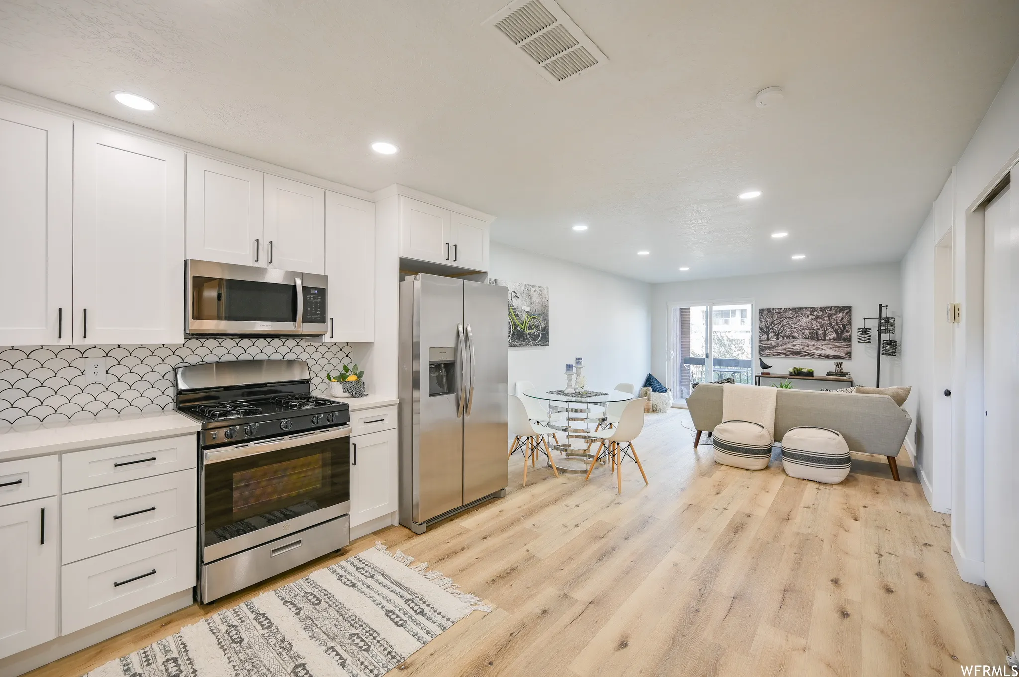 Open-concept living space featuring a modern kitchen with white cabinetry, stainless steel appliances, and a unique tile backsplash