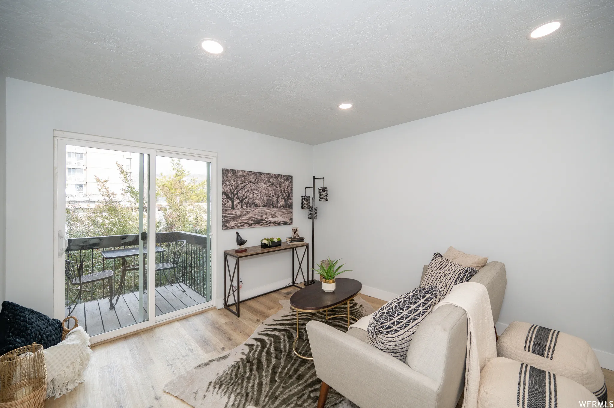 Living area featuring light wood-finish flooring, recessed lighting, and a glass sliding door opening to a private balcony