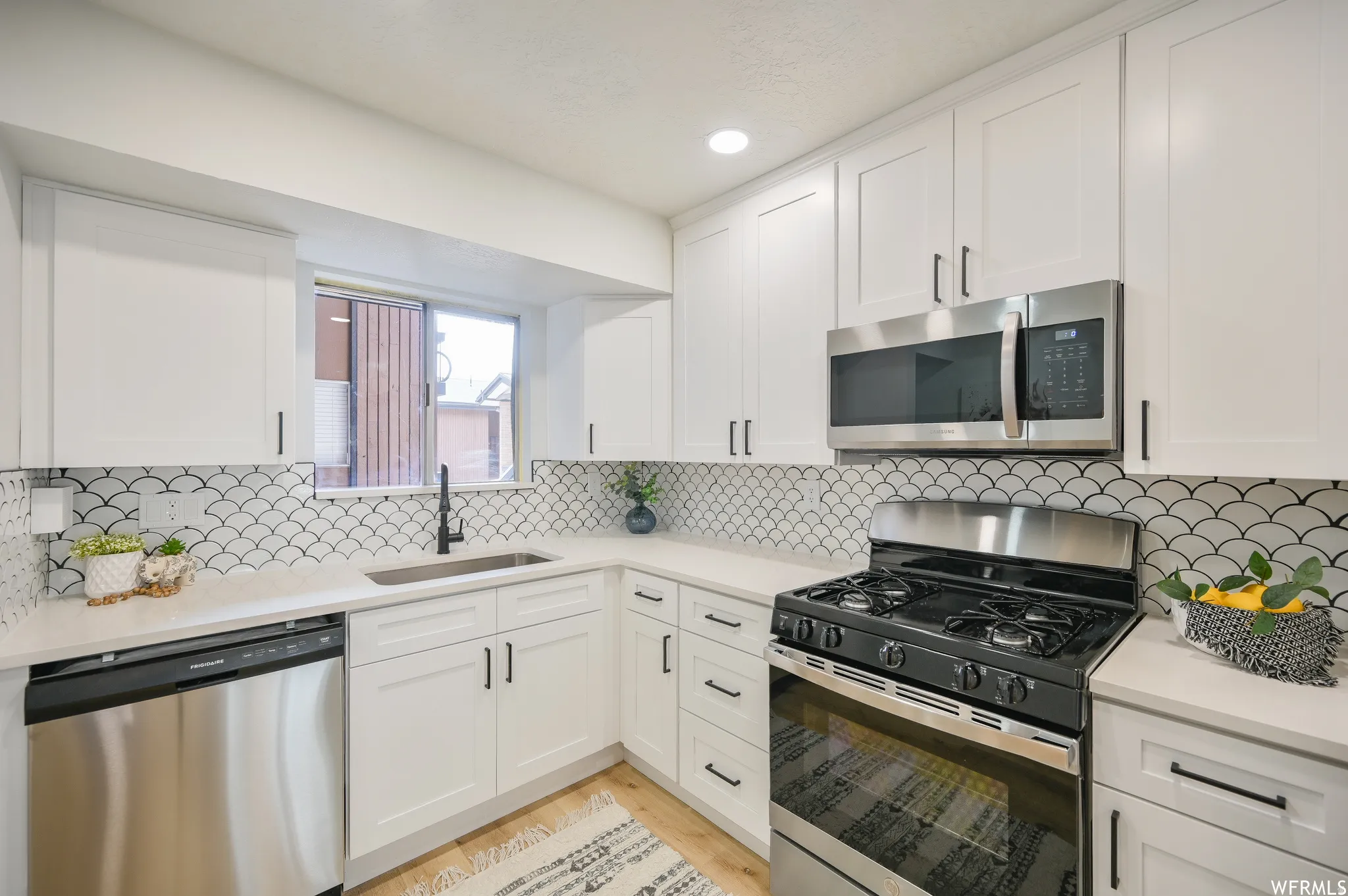 Modern kitchen featuring white shaker cabinetry, stainless steel appliances, and a unique scallop-patterned backsplash