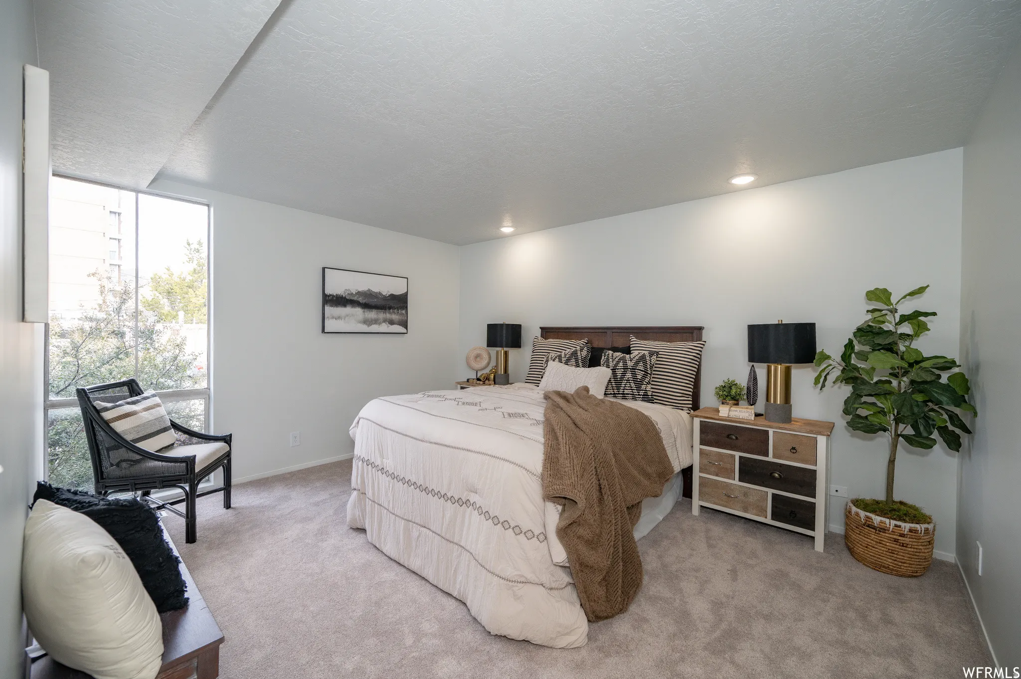 Spacious room featuring broad windows with views of exterior trees, plush carpet flooring, recessed lighting, and a dark wood headboard