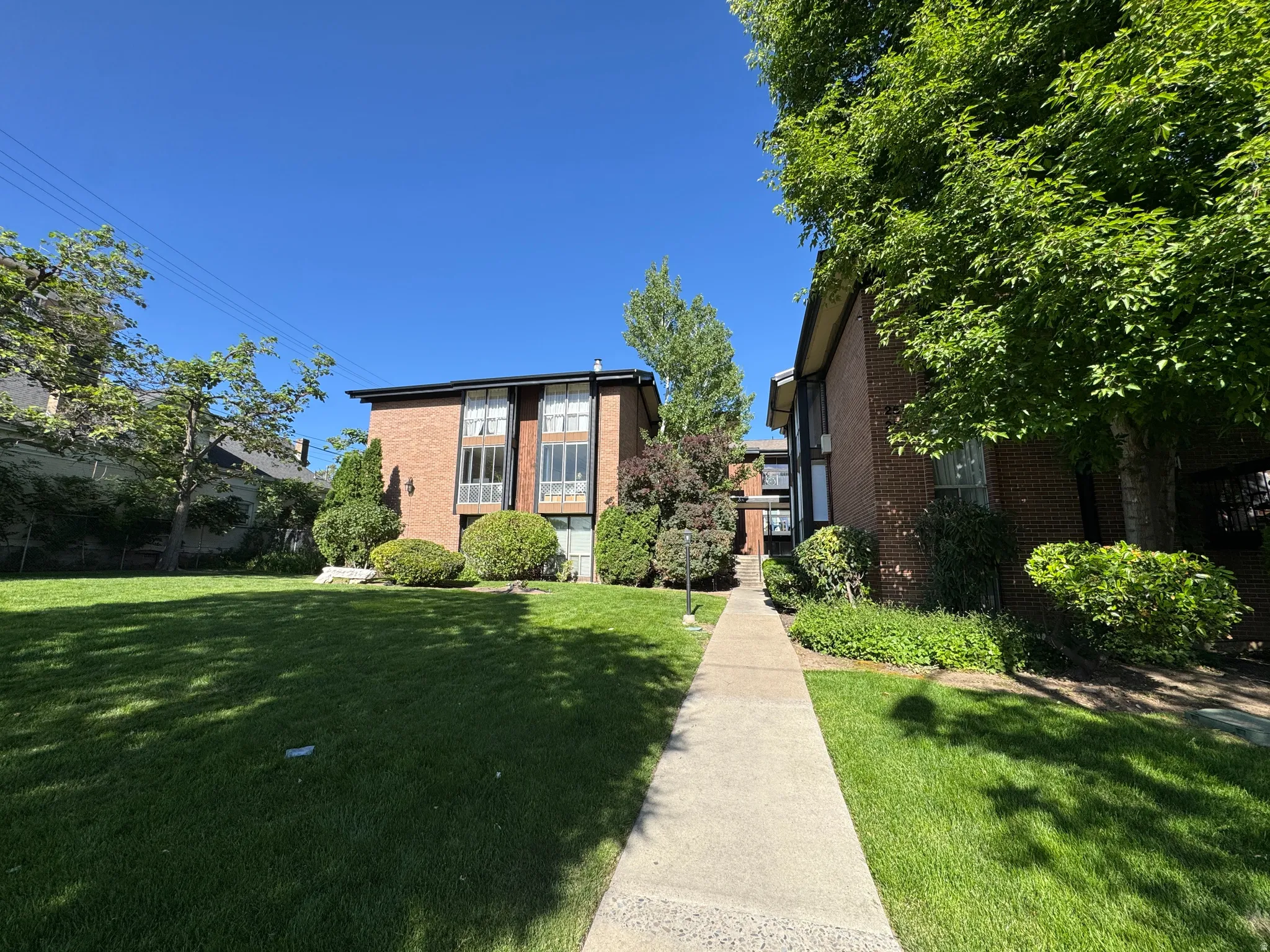Brick apartment building with multiple levels, featuring large windows and established landscaping