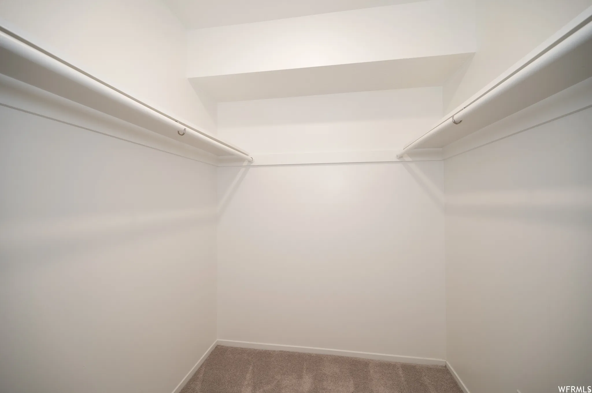 Walk-in closet featuring light-colored walls, overhead shelving, dual hanging rods, and neutral-toned carpeting