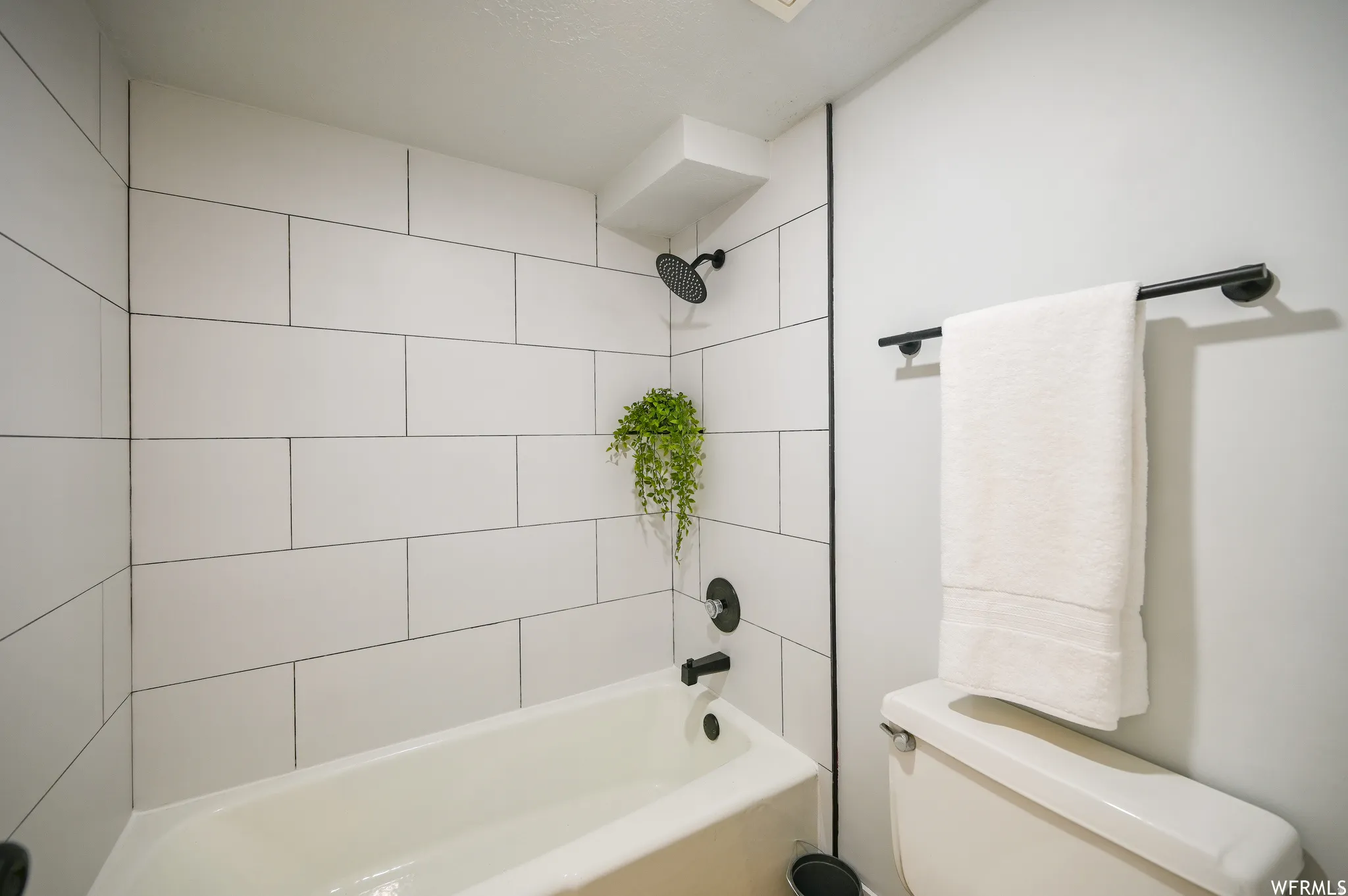 Bathroom tub and shower combination featuring white subway tile surround, matte black shower fixtures, and a white porcelain tub