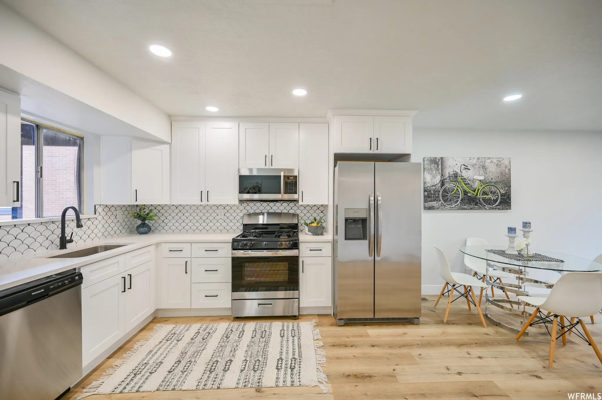 Modern kitchen featuring white shaker cabinetry, stainless steel appliances, a unique scalloped tile backsplash, recessed lighting, and wood-finish flooring