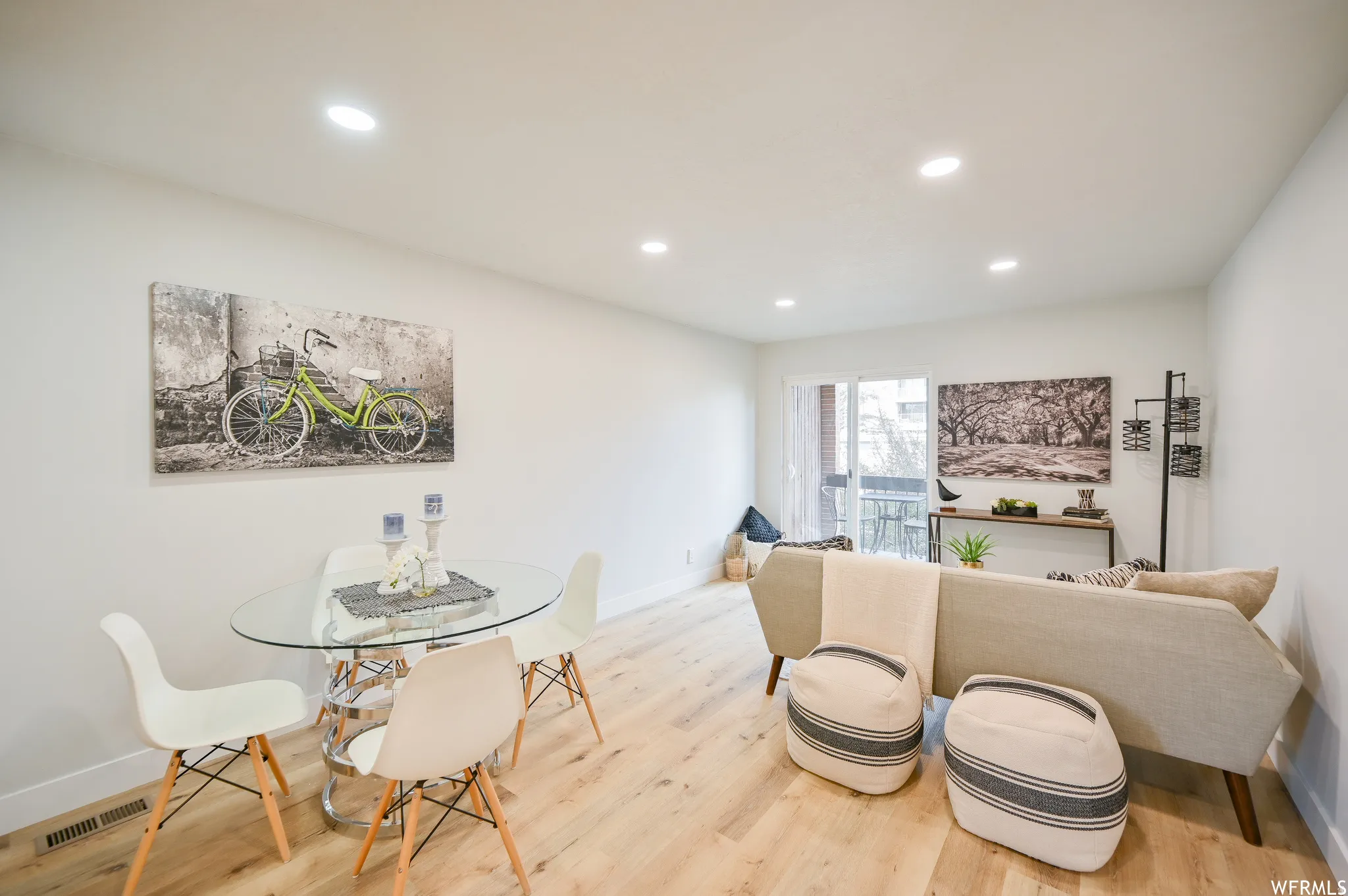 Open-concept living space with light wood-finish flooring, recessed lighting, and a sliding glass door leading to an exterior balcony