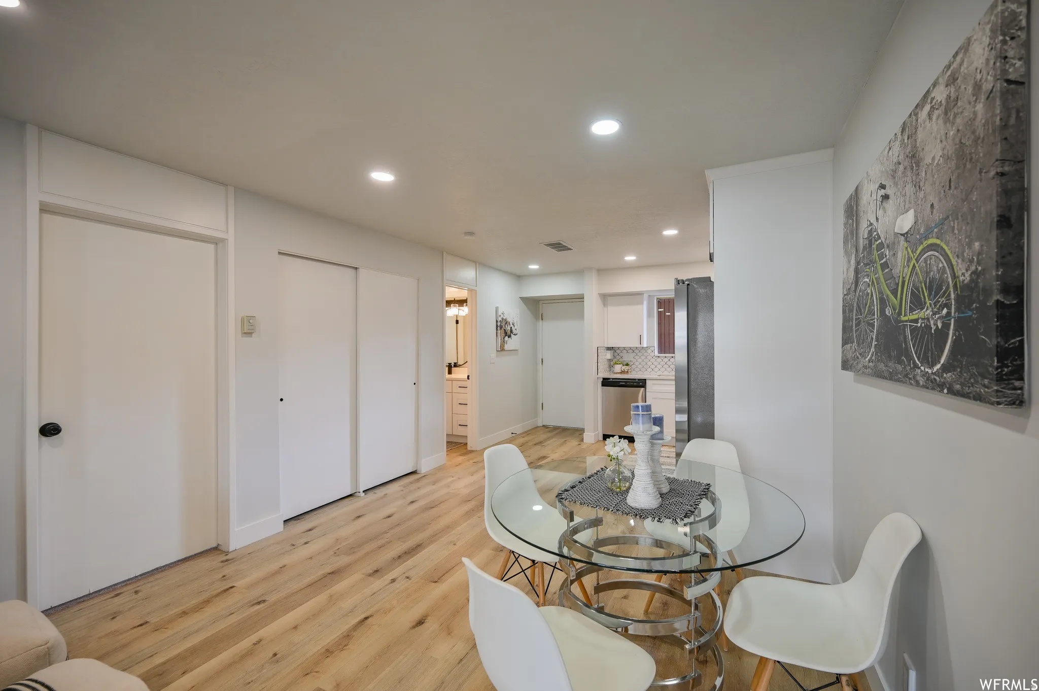Open-concept living area featuring wood-finish flooring, recessed lighting, and a glass-top dining table