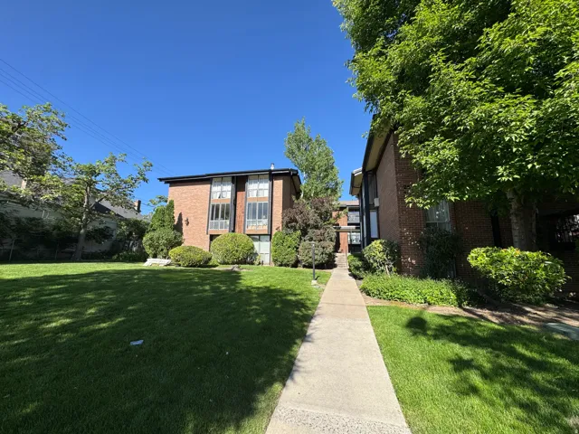 Brick apartment building with multiple levels, featuring large windows and established landscaping