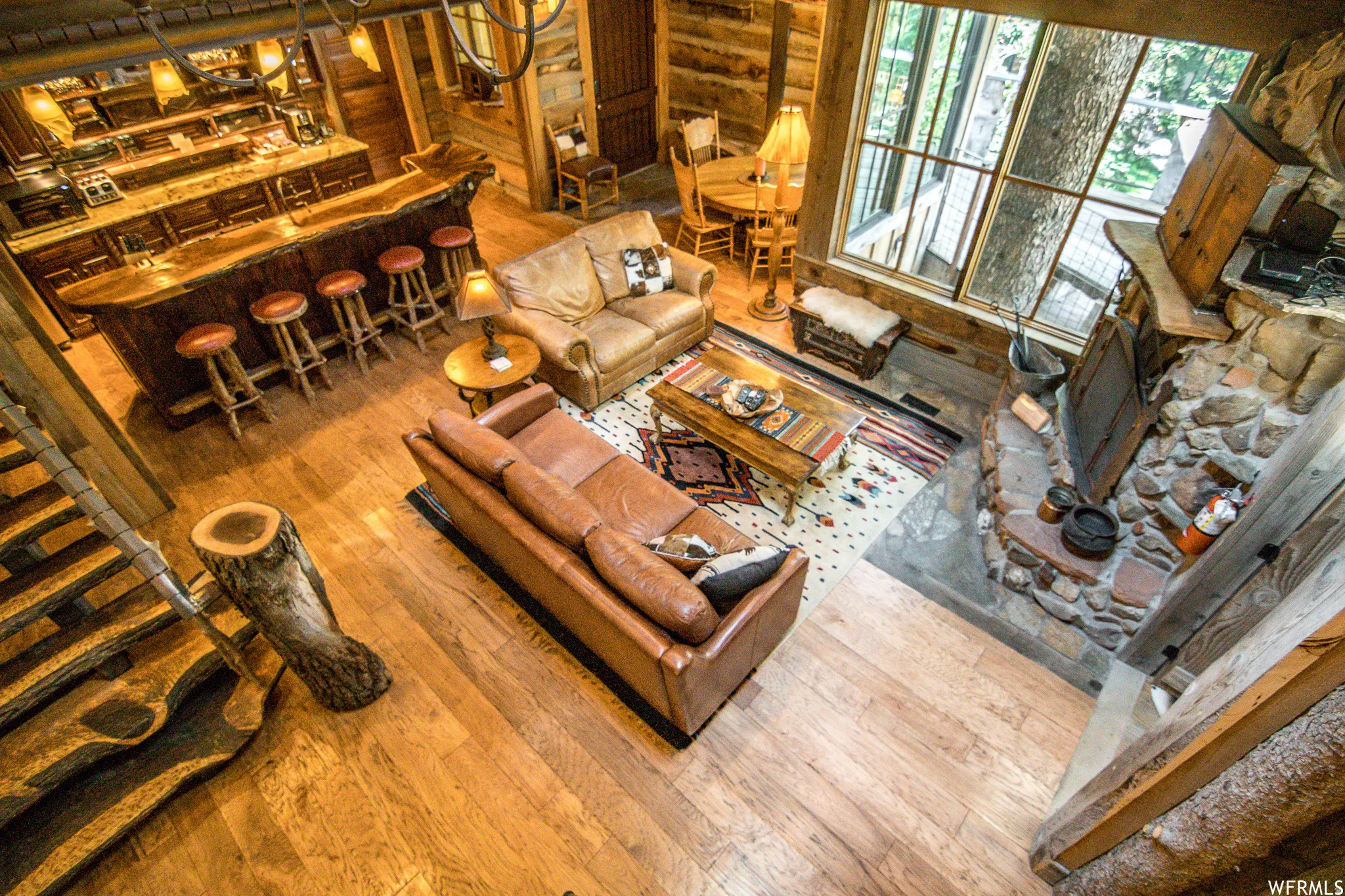 Spacious living area featuring wood-finish flooring, a prominent stone fireplace, and a large window wall