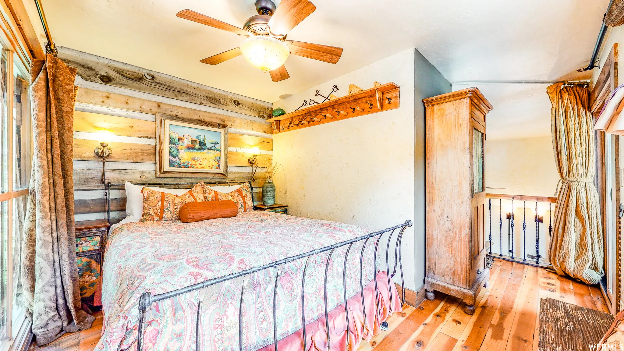 Bedroom featuring a log-style accent wall, wood-finish flooring, and a ceiling fan with integrated lighting