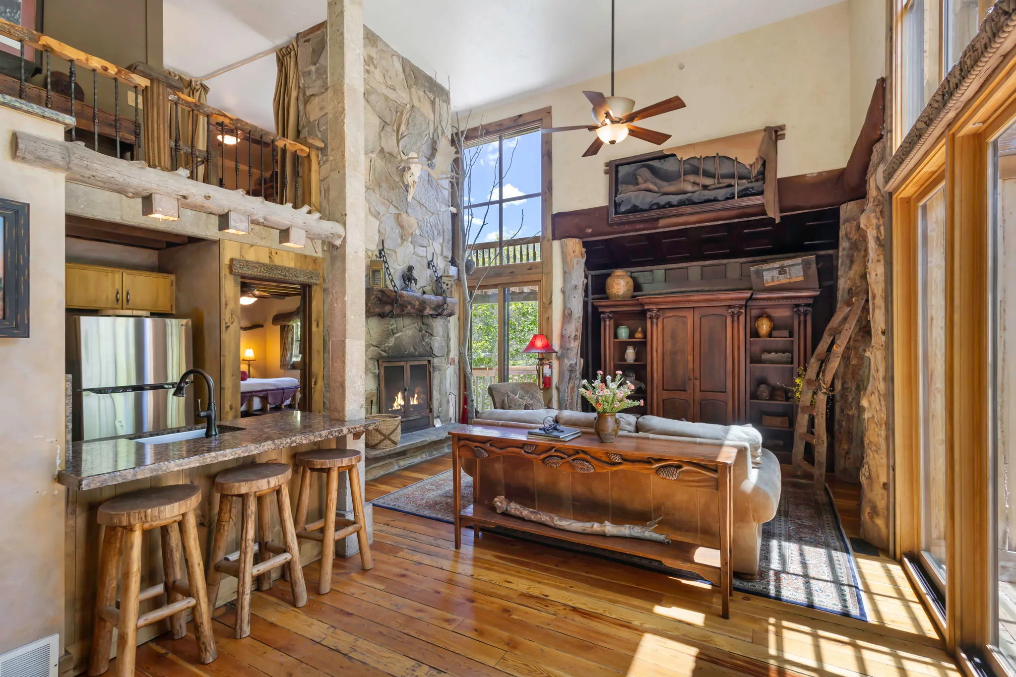 Spacious living area featuring a stone fireplace, high ceilings, large windows, wood-finish flooring, and a built-in media center