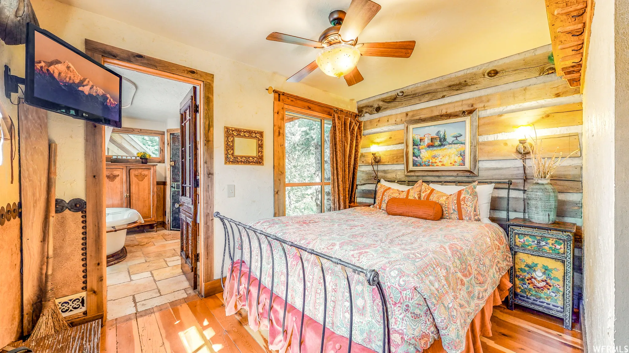 Bedroom featuring wood-finish flooring, a decorative wood accent wall with sconce lighting, and a ceiling fan