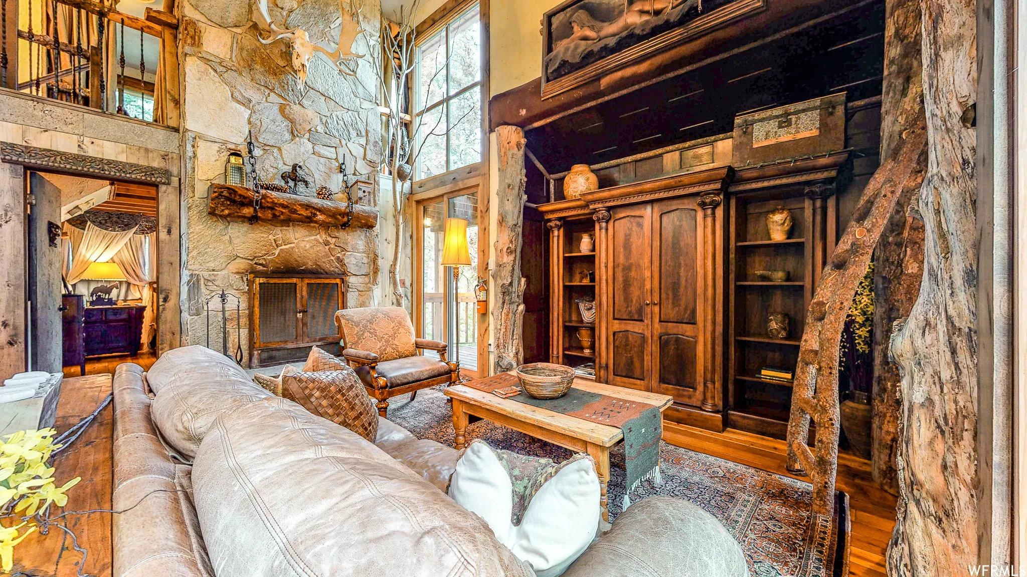 Great room featuring a floor-to-ceiling stone fireplace with a substantial timber mantel, large windows providing natural light, and natural wood structural elements
