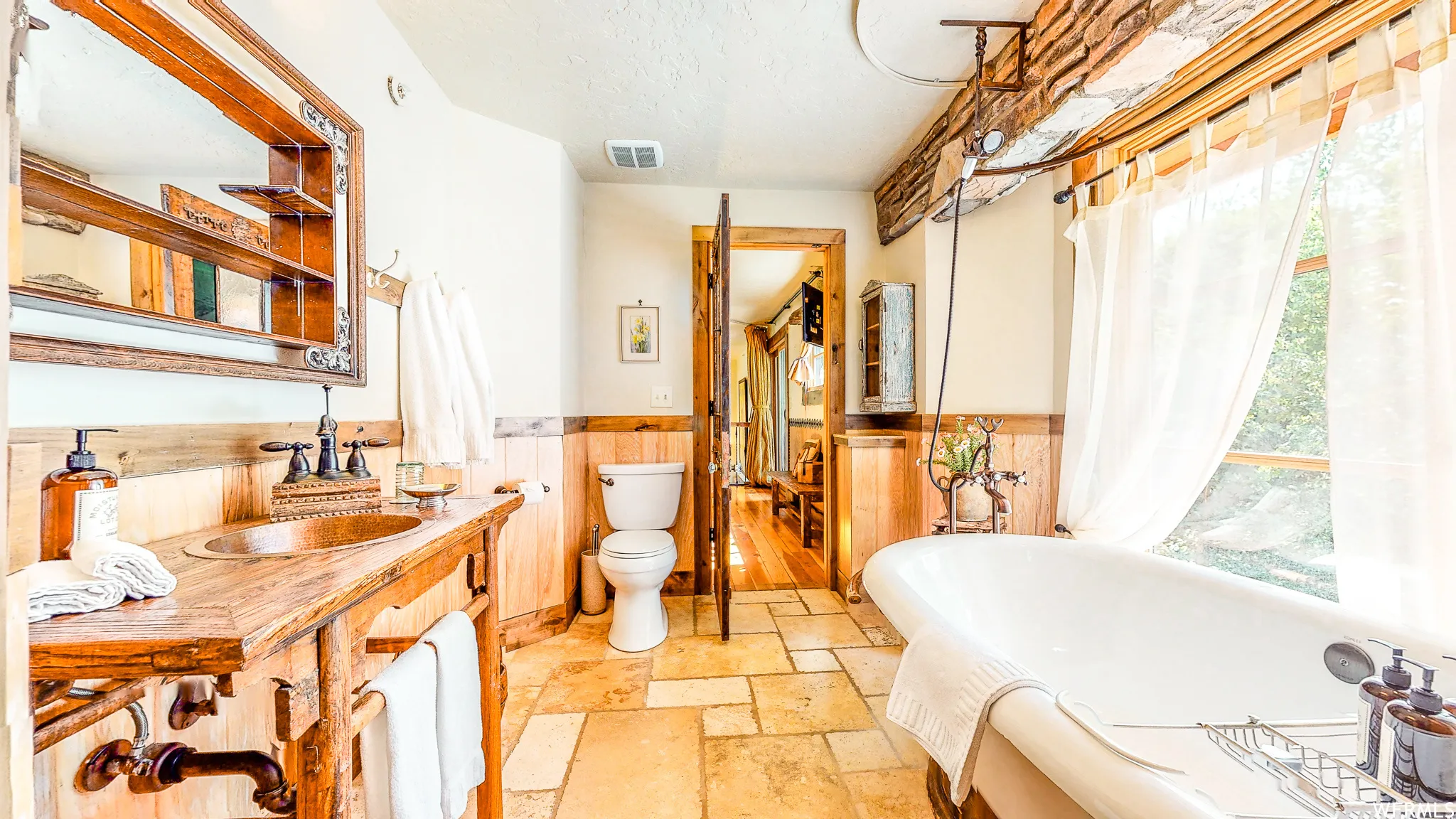 Bathroom featuring a freestanding clawfoot tub, a wood-finish vanity with a copper basin sink, and wood-paneled walls