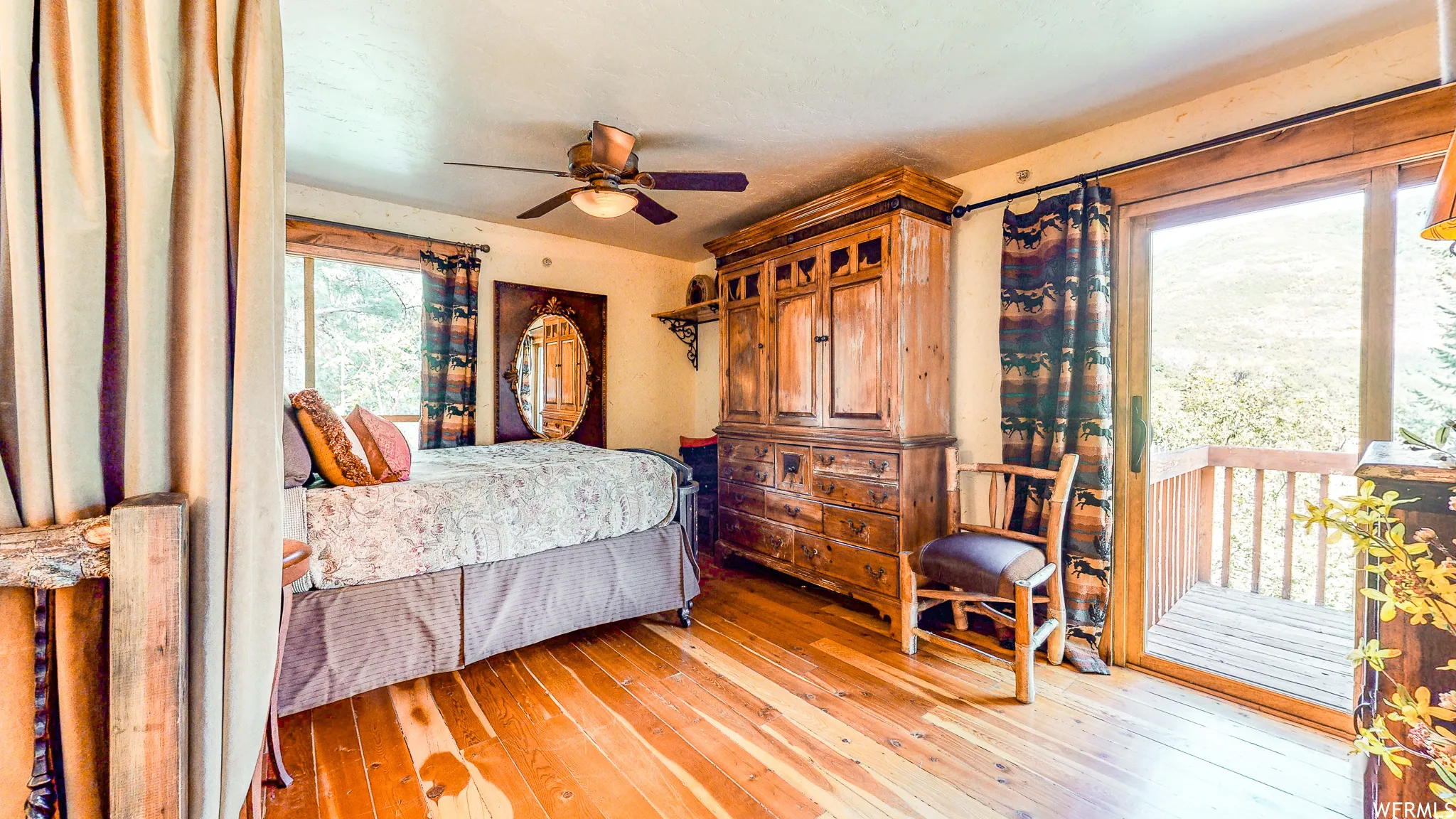 Warm wood-finish flooring, a ceiling fan with integrated lighting, and a sliding glass door leading to an outdoor balcony
