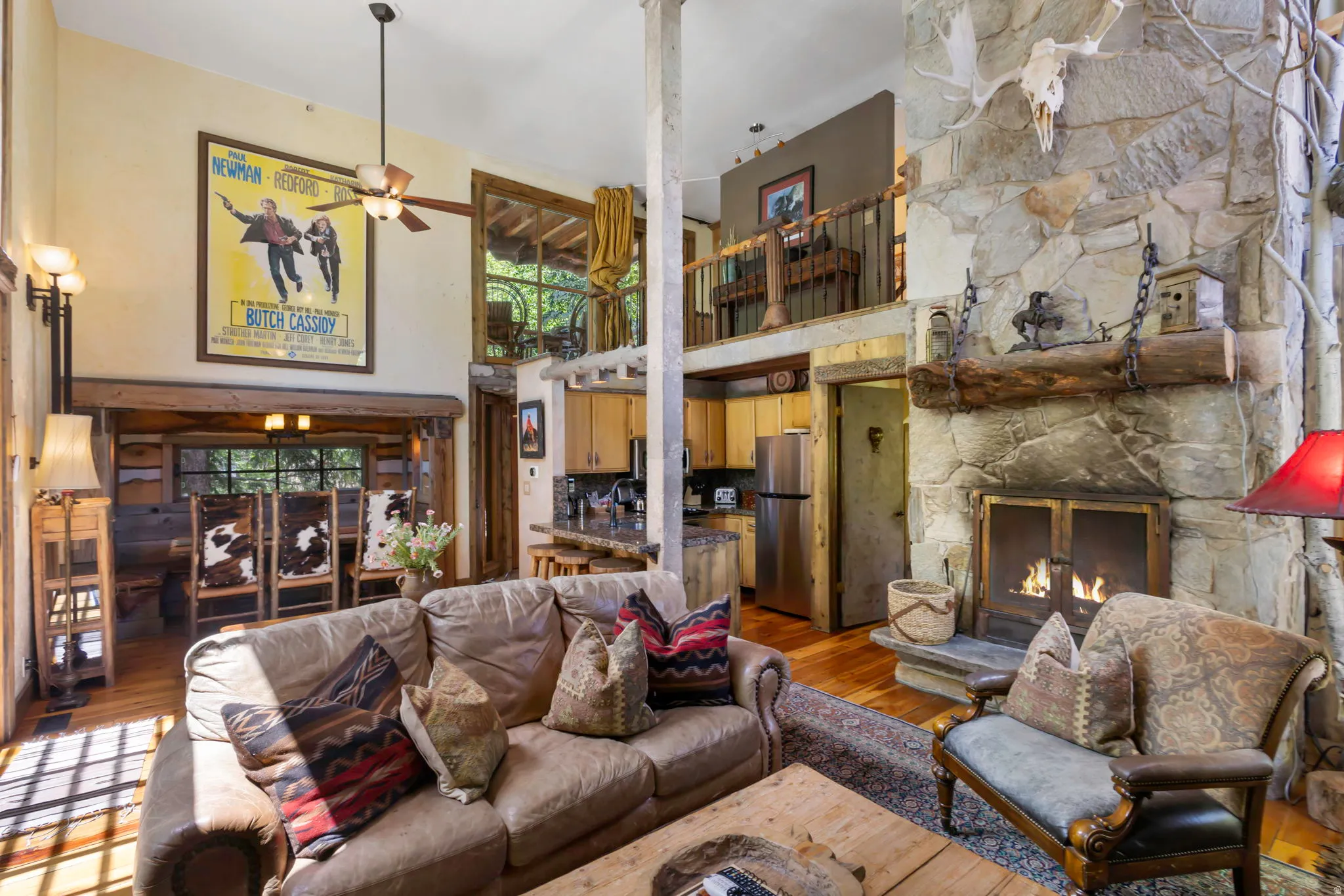 Open-concept living space featuring a floor-to-ceiling stone fireplace with a wood mantle, hardwood flooring, and a second-story balcony overlooking the room