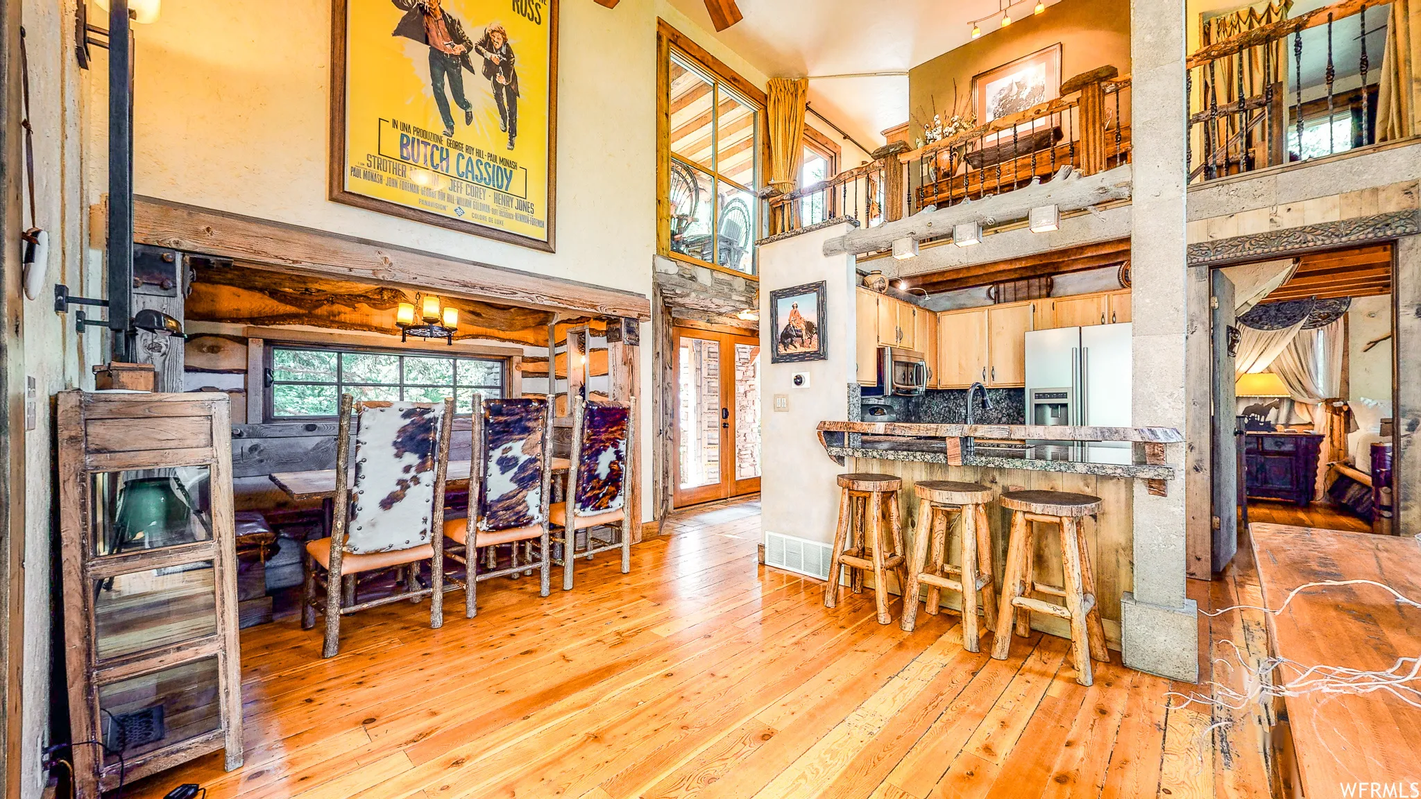 Open-concept living space with wood-finish flooring, a kitchen featuring a breakfast bar with stone accents, an adjacent dining area, and a lofted upper level with an iron railing