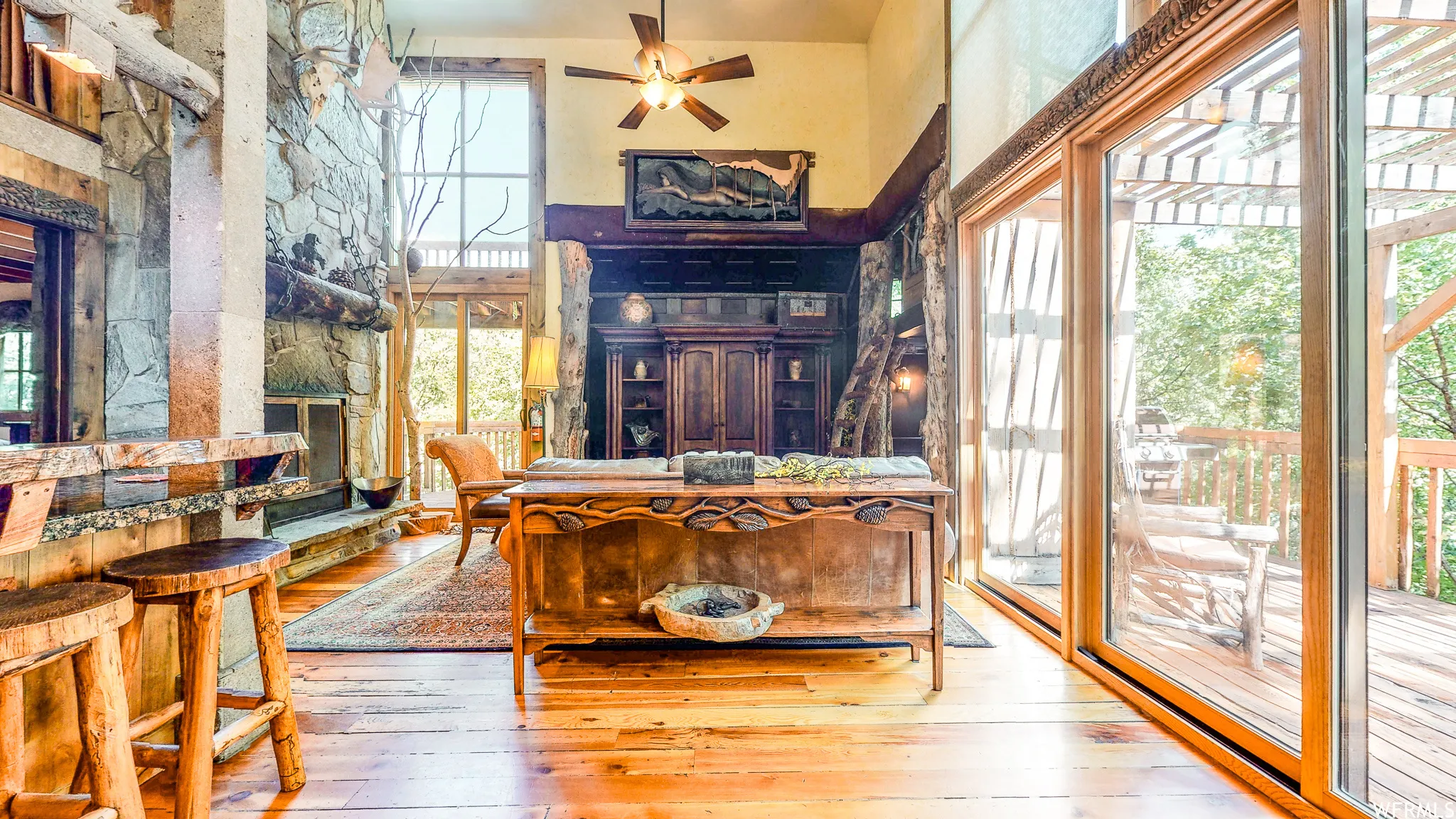 Spacious room featuring wood-finish flooring, a stone-clad fireplace, and expansive floor-to-ceiling windows