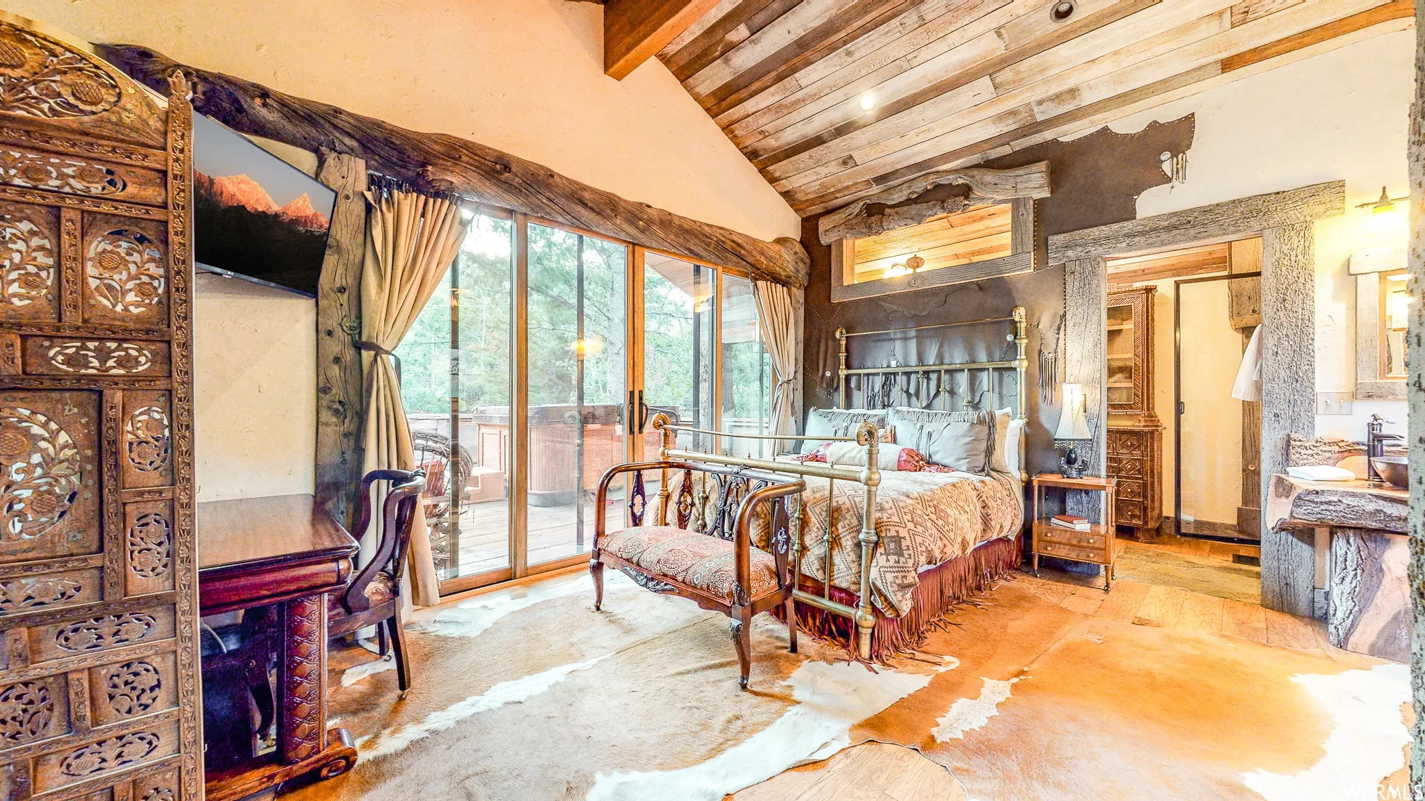 Vaulted wood plank ceiling over a bedroom featuring sliding glass doors, a brass bed frame, and a carved wood screen