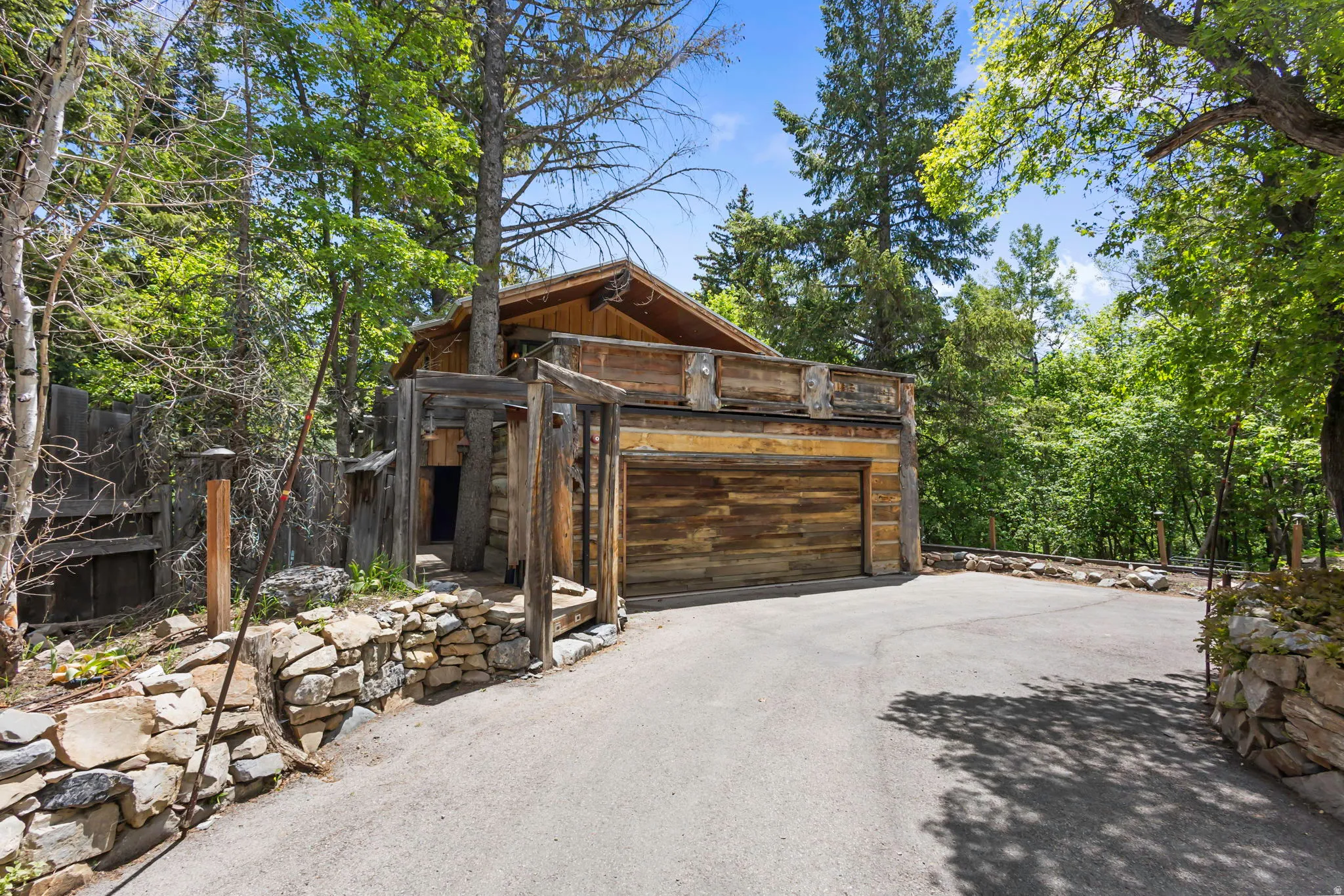 Integrated garage with wood-finish door, extensive paved driveway, and stone retaining walls