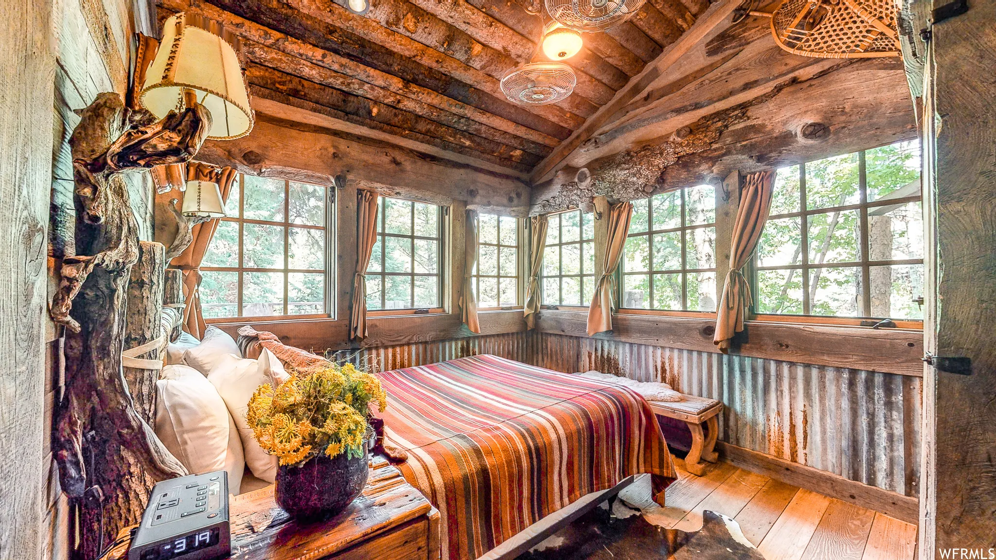 Window-lined room featuring exposed natural wood beams, plank wood flooring, corrugated metal wainscoting, and built-in wall sconces