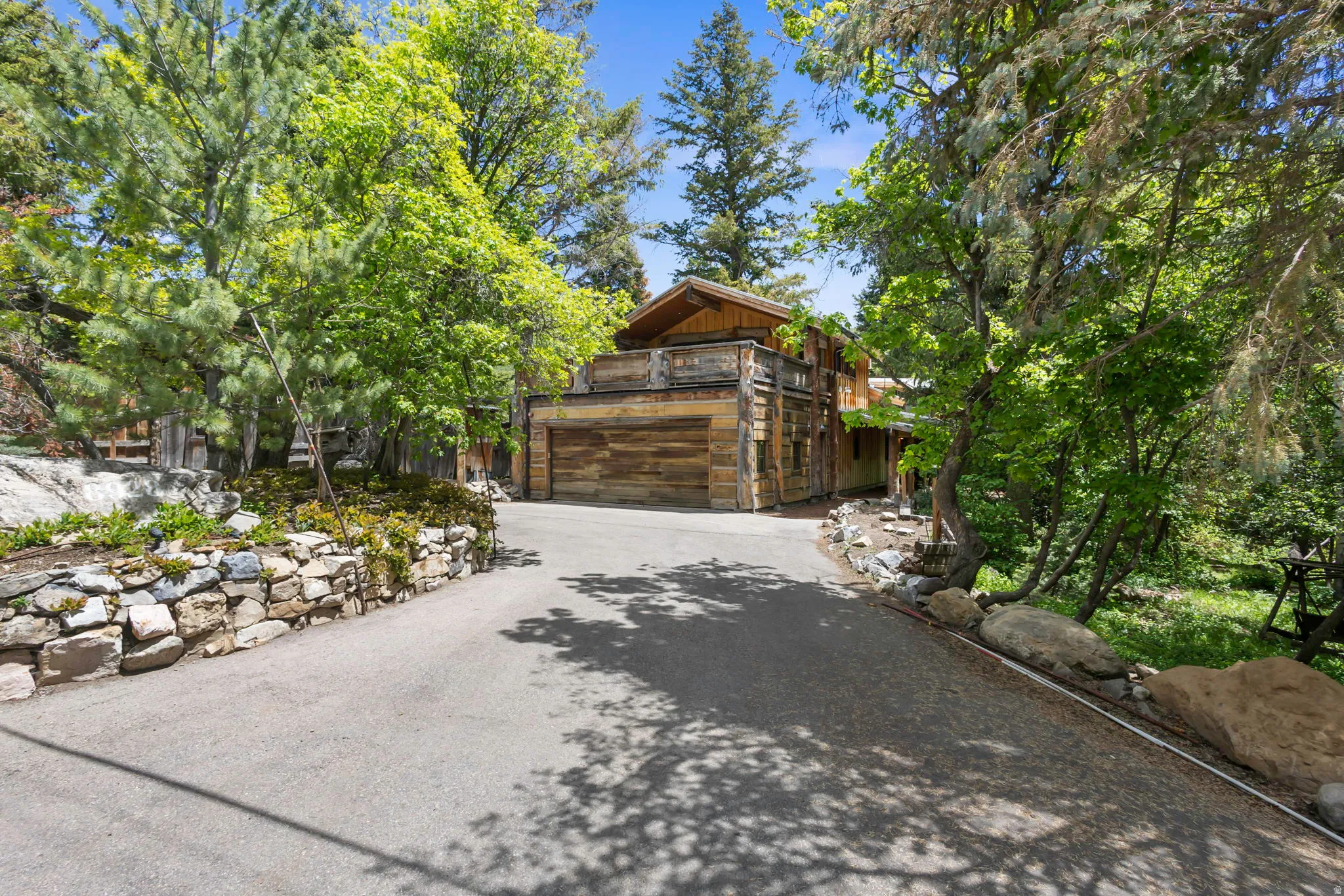 Asphalt driveway curving towards a multi-level wood-sided residence with an integrated garage