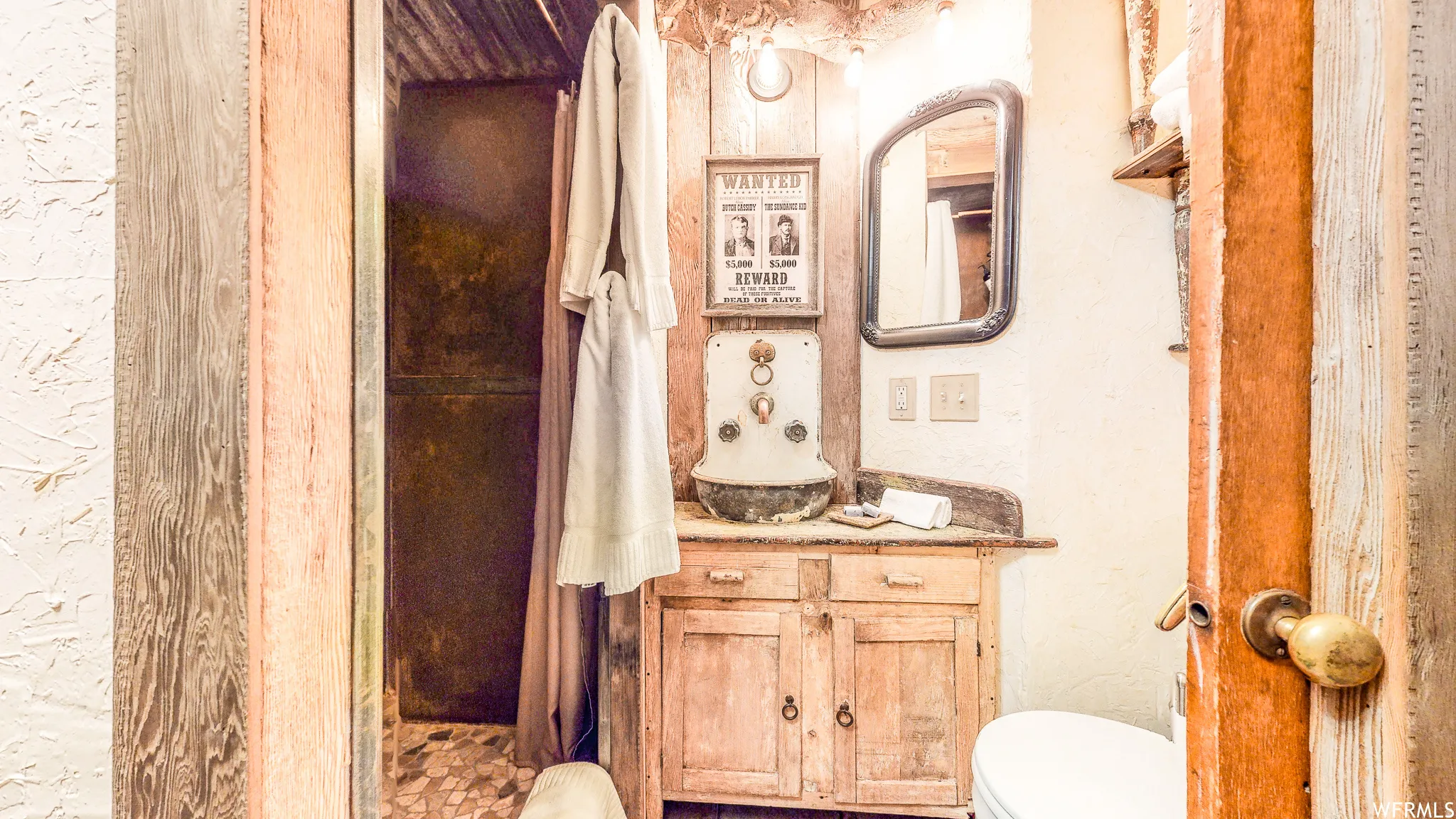 Bathroom featuring a rustic wood vanity with integrated basin, framed wall mirror, and an adjacent shower enclosure with a dark curtain