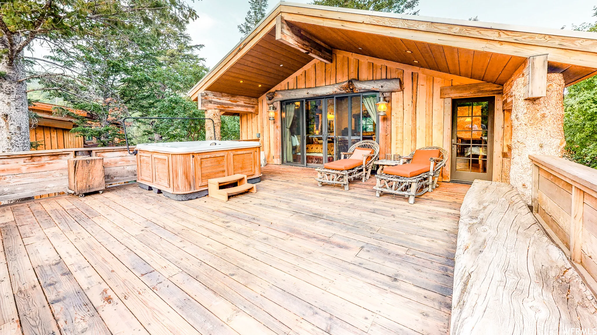 Expansive wood deck with a built-in hot tub, wooden railing, and direct access to the interior via a glass-paneled door and large sliding glass doors