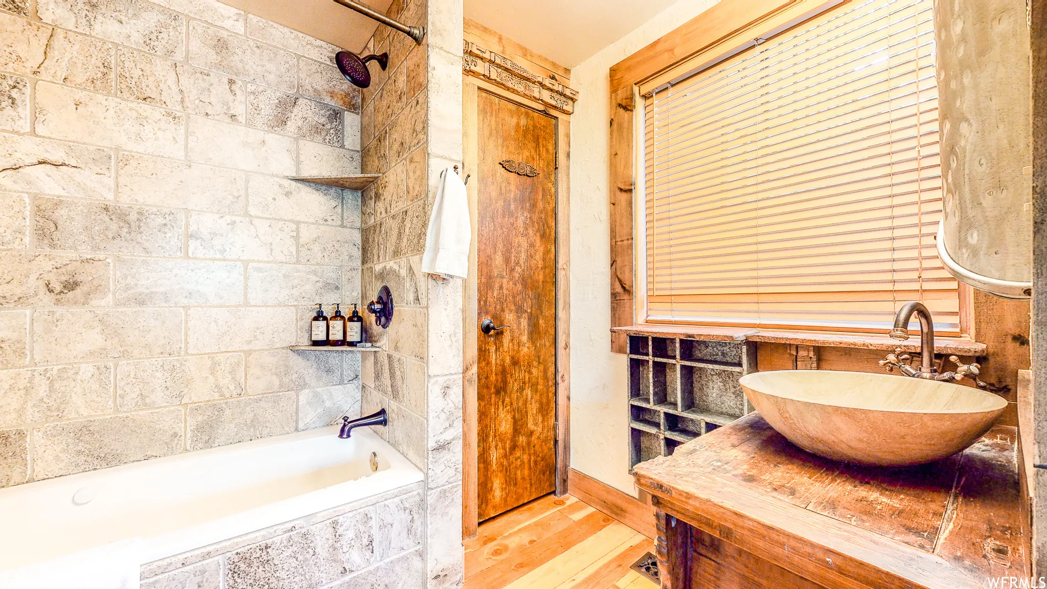 Bathroom featuring a soaking tub with stone tile surround, shower with oil-rubbed bronze fixtures, a natural wood vessel sink, and a wood-finish vanity with open shelving
