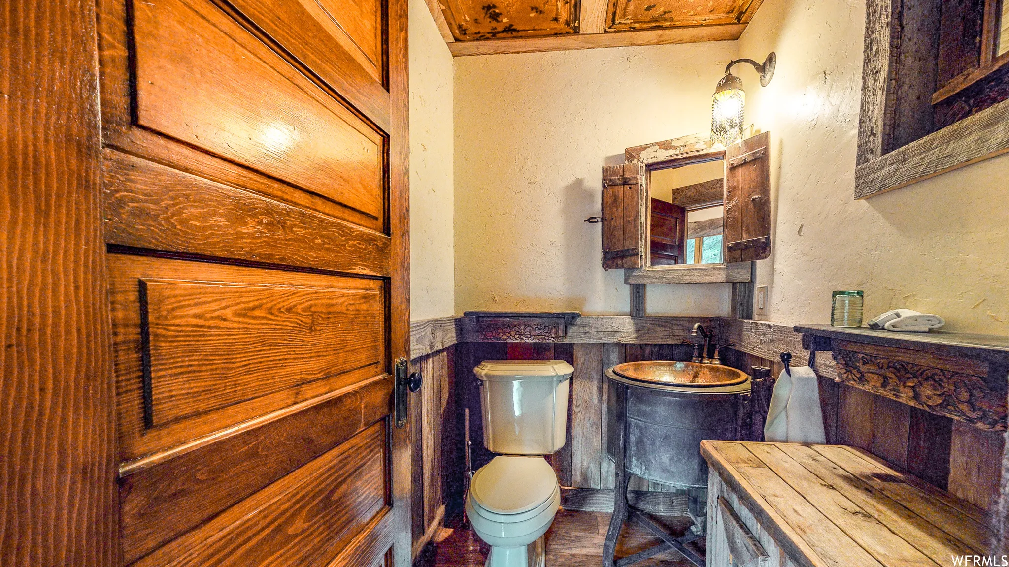 Powder room featuring a copper vessel sink, rustic wood vanity, wall-mounted sconce lighting, and wood paneling