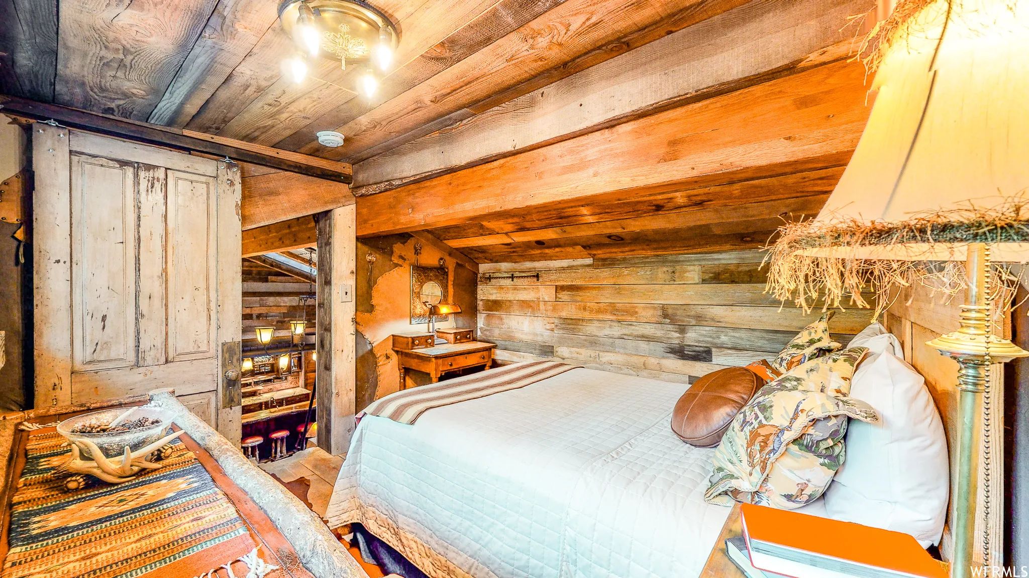 Attic bedroom featuring exposed wood beam ceiling, wood-paneled walls, barn door access, and a built-in wooden nightstand